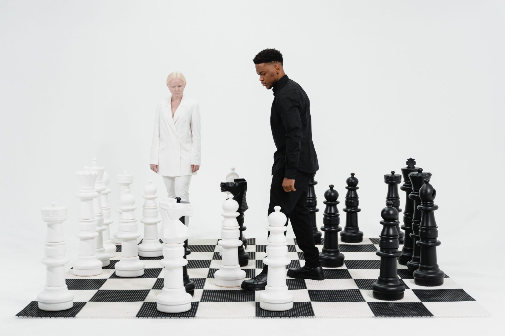 Two people facing off on a giant chessboard, black vs white