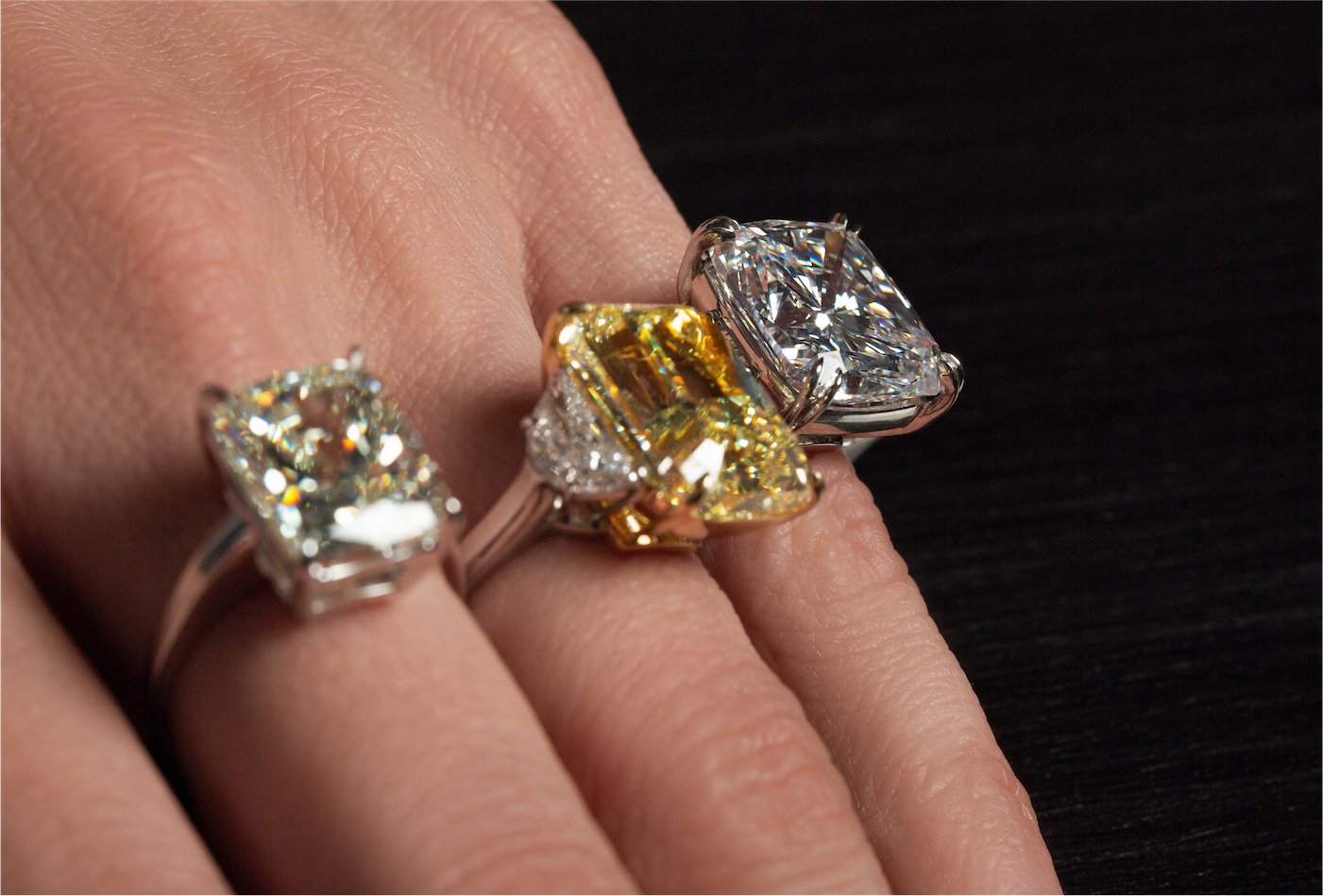 Three large diamond solitaire engagement rings including a fancy yellow diamond on a hand