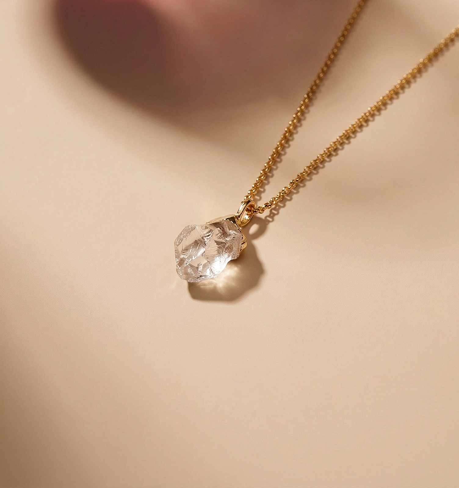 Raw clear-crystal pendant on a gold chain worn at the neckline, soft editorial lighting
